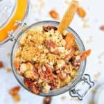 peanut butter granola in a large glass jar with wooden spoon