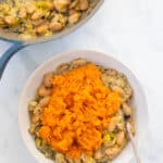 closeup of this Gluten-Free and Vegan Butterbean and Leek Pie topped with sweet potato mash in a white bowl with a silver spoon on a marble countertop.