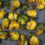 crispy brussel sprouts on grey baking tray with herbs on top.