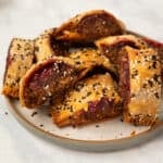 homemade lentil and walnut sausage rolls on a stoneware plate garnished with sesame seeds.