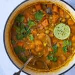 Sweet Potato Satay Curry displayed in a large pot with serving spoon. Pot is displayed on white marble background