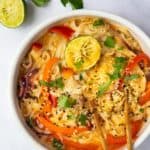 Thai Curry Noodle Soup in a bowl with chopsticks, displayed on a white marble background with lime and coriander.