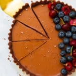 overhead of vegan chocolate tart sliced with golden cake slice and topped with berries.