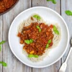 Spaghetti Bolognese topped with fresh basil in a bowl. Bowl is on a wooden background.