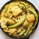 Cooked Cauliflower Cheese in black skillet pan. Pan is displayed on white marble background
