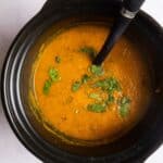 Overhead shot of blended carrot and coriander soup in slow cooker topped with fresh coriander and ladle.