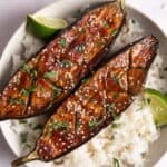 2 miso-glazed aubergines on a bed of white rice with lime wedges. The white bowl is on a white surface.