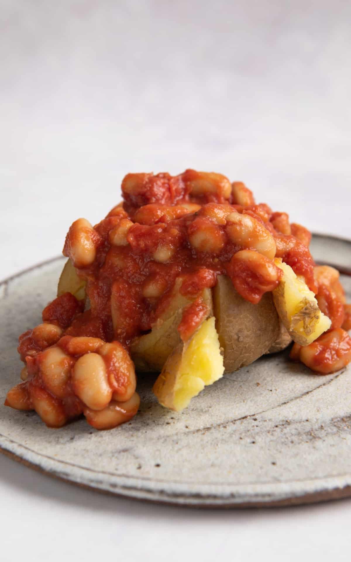 slow cooker jacket potato cut open and topped with homemade beans served on a grey plate