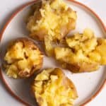 4 jacket potatoes cut open on a plate with melted butter on top.