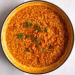 overhead shot of tomato risotto in large shallow frying pan on white surface.