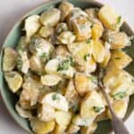 potato salad in green bowl with beige rim. Bowl is on white surface.