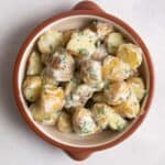 overhead shot of potato salad in brown/orange bowl on white surface.