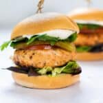 salmon burger with bun and lettuce on white background.