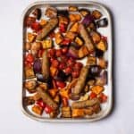 Sausages baked on the tray with colourful vegetables.