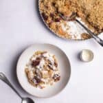 apple and blackberry crumble on a marble background served with cream.