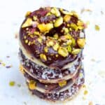 4 doughnuts stacked on a white marble background with pistachio and coconut toppings.