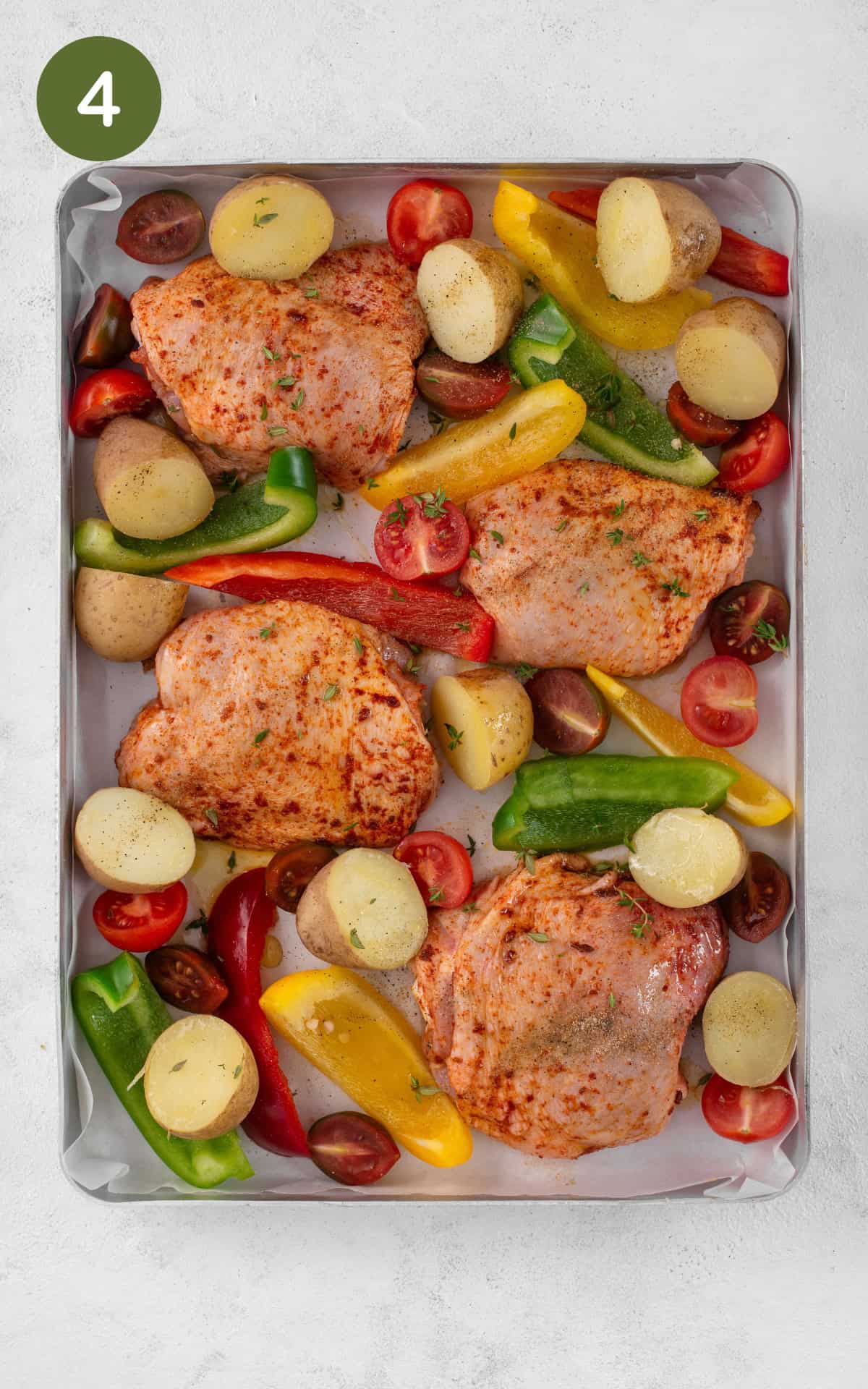 Vegetables and chicken thighs on a baking tray.