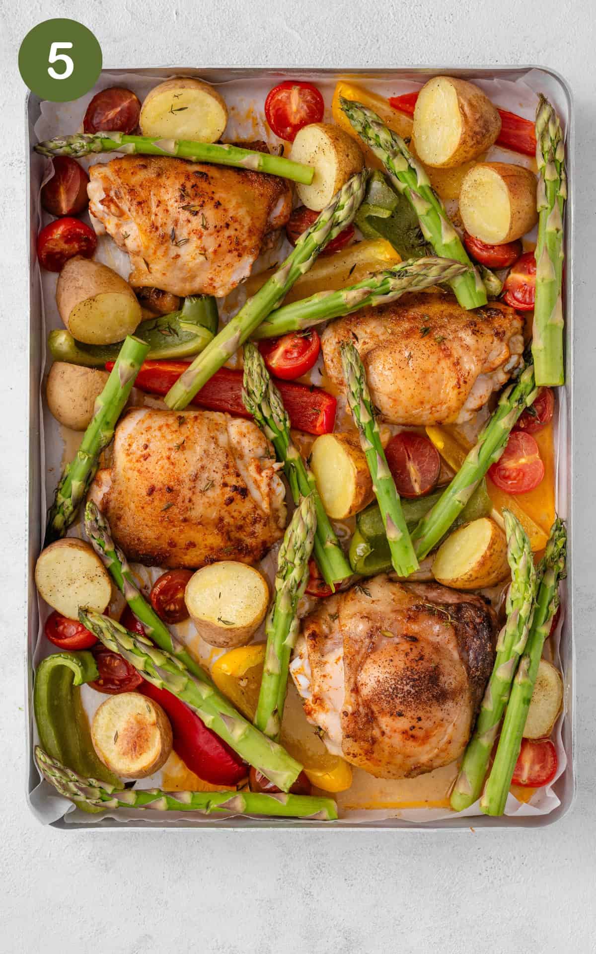 Chicken thighs, asparagus and other vegetables on a baking tray.