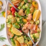 Smoked salmon salad served on a plate with lemon slices and herbs on top.
